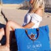 Femme assise sur une terrasse en bois à la plage avec un grand sac cabas de plage bleu roi Sel de Mer
