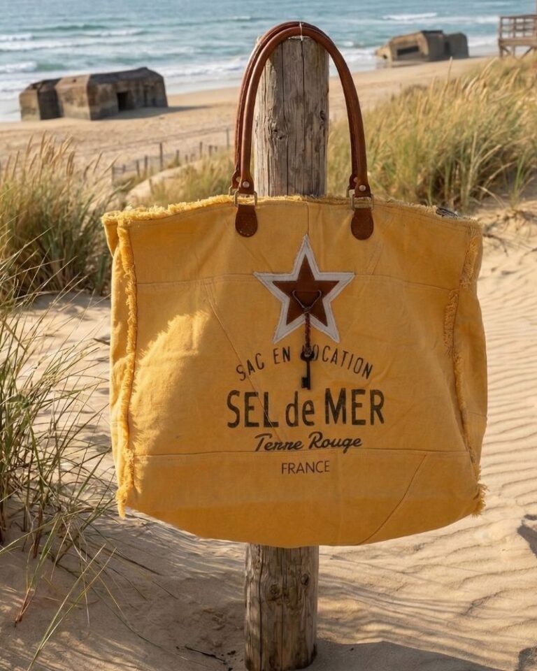 sac plage xl jaune Grand sac cabas Sel de Mer en toile recyclée jaune safran suspendu à un poteau en bois sur une plage landaise. Détails en cuir et impression vintage sur le devant