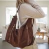 Sac en daim marron porté à l'épaule, style bohème chic avec poches zippées